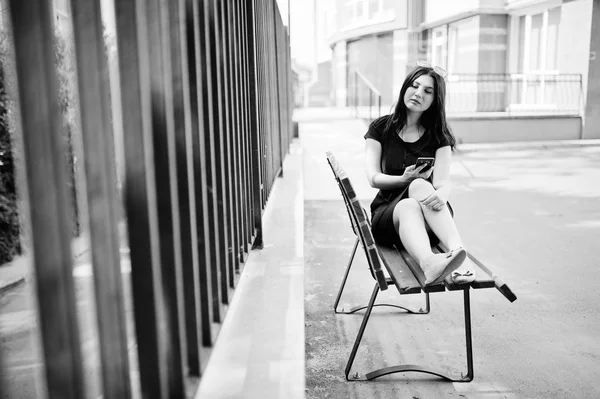 Brunetka dziewczyna w czarnej sukni, Okulary przeciwsłoneczne, siedząc na ławce, liste — Zdjęcie stockowe