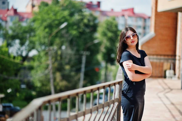 Ruskeaverikkö tyttö musta mekko, aurinkolasit poseeraa kadulla cit — kuvapankkivalokuva