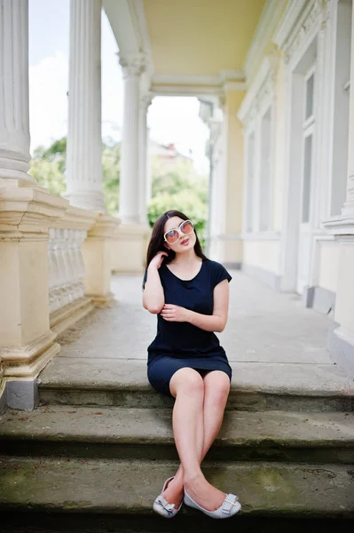 Brunett tjej på svart klänning, solglasögon sitter på trappan till ol — Stockfoto
