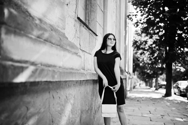 Brunette fille à robe noire sur lunettes de soleil avec sac à main à portée de main — Photo