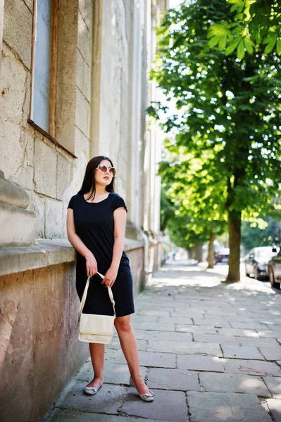 Brunette fille à robe noire sur lunettes de soleil avec sac à main à portée de main — Photo