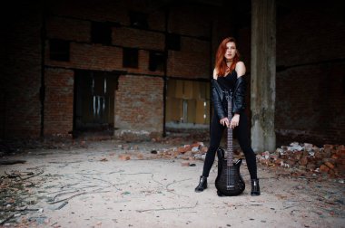 Red haired punk girl wear on black with bass guitar at abadoned  clipart