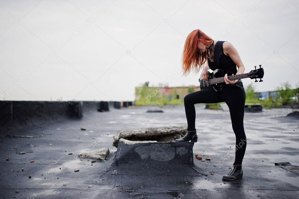 Red haired punk girl wear on black with bass guitar at the roof.