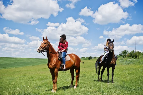 Tow jonge mooie meisjes een paarden rijden op een veld op een zonnige dag — Stockfoto