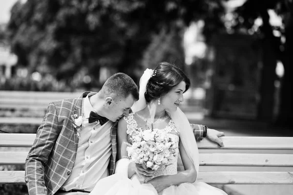 Beautiful wedding couple sitting on a bench in the city centre o — Stock Photo, Image