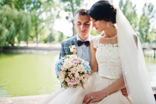 Wunderbar aussehendes Hochzeitspaar sitzt am See auf der Sonne — Stockfoto