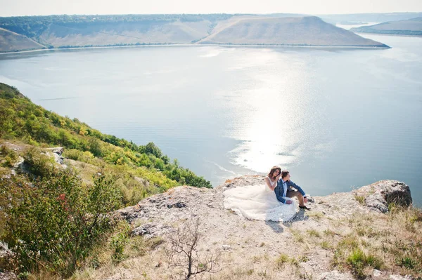 W の崖の端に座っている若い結婚式のカップルを見事な — ストック写真