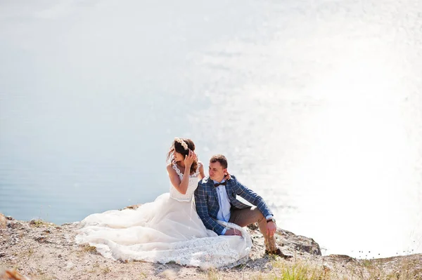 Stunning young wedding couple sitting on the edge of the cliff w — Stock Photo, Image