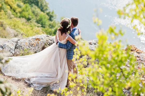 Recém-casado de pé ao lado de arbustos verdes no precipício com um v — Fotografia de Stock