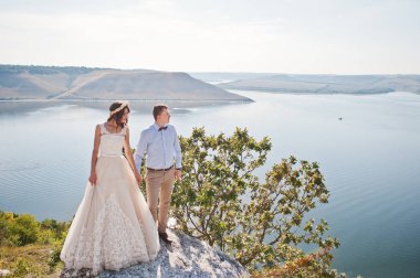 V ile uçurumun üzerinde yeşil çalılar yanında duran yeni evli