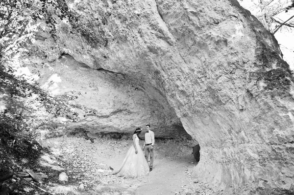 Beautiful bride with handsome groom posing next to the cave in f — Stock Photo, Image