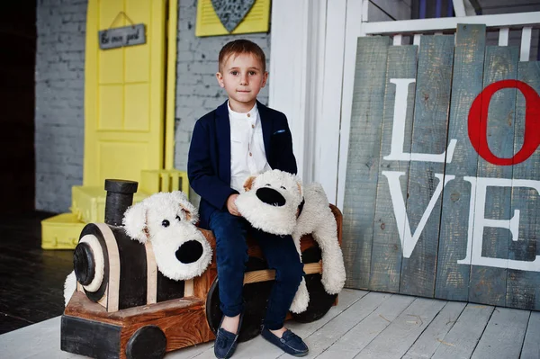 Kleiner hübscher Junge stilvoll gekleidet posiert auf der Spielzeugeisenbahn. — Stockfoto