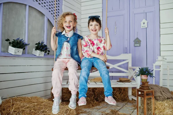 Two little girls sitting on the swing outside the house with str