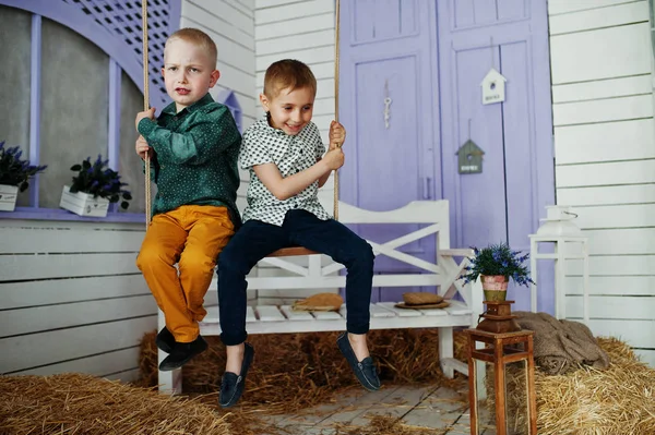 Dos niños pequeños sentados en el swin fuera de la casa con paja — Foto de Stock