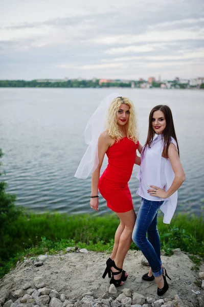 Impressionante noiva em vestido vermelho posando com sua dama de honra no lago — Fotografia de Stock