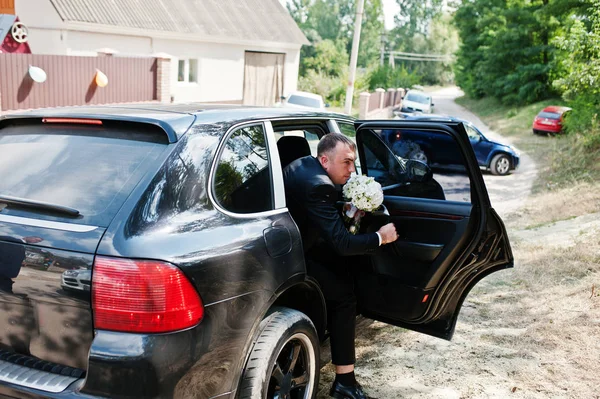 Knappe bruidegom lopen van de koele ingerichte bruiloft suv wit — Stockfoto