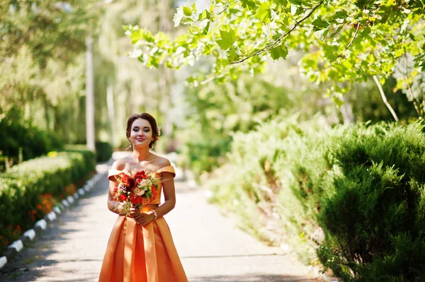 Atraente dama de honra em vestido laranja posando com buquê de noiva — Fotografia de Stock