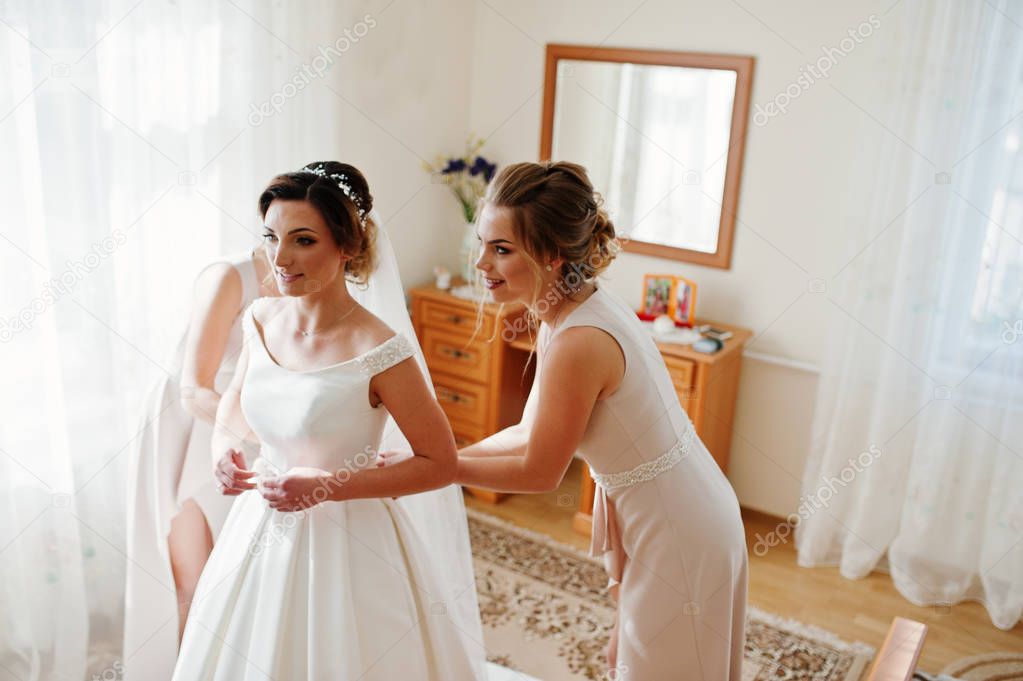 Bridesmaids helping gorgeous bride to dress up and get ready for