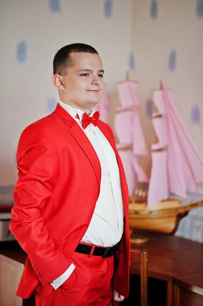 Yakışıklı damat kırmızı smokin odasında bir düğün gününde poz — Stok fotoğraf