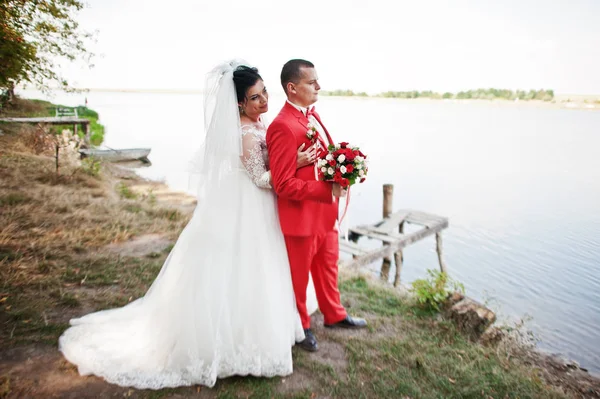 Prachtige bruidspaar met een boeket knuffelen op de oever van het meer. — Stockfoto