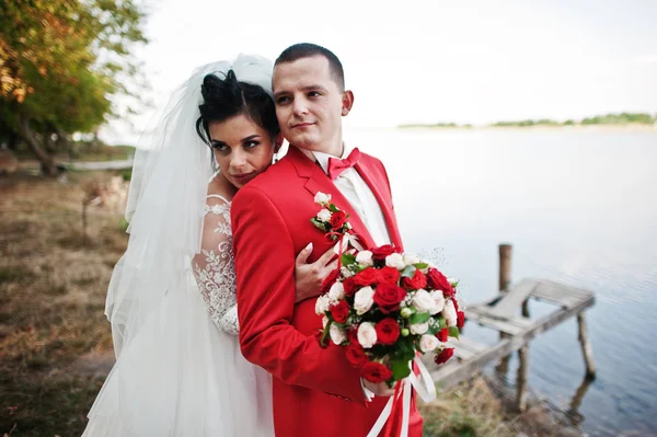Приголомшлива весільна пара з букетом, що обіймається на березі озера . — стокове фото