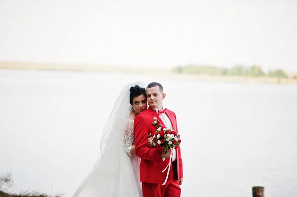 Atemberaubendes Hochzeitspaar mit einem Strauß, der sich am Seeufer umarmt. — Stockfoto