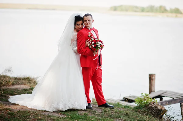 Prachtige bruidspaar met een boeket knuffelen op de oever van het meer. — Stockfoto