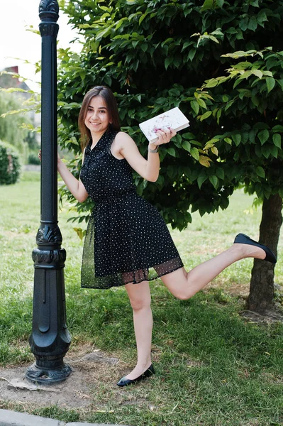 Portrait of a shy young woman in black polka dot dress holding b — Stock Photo, Image