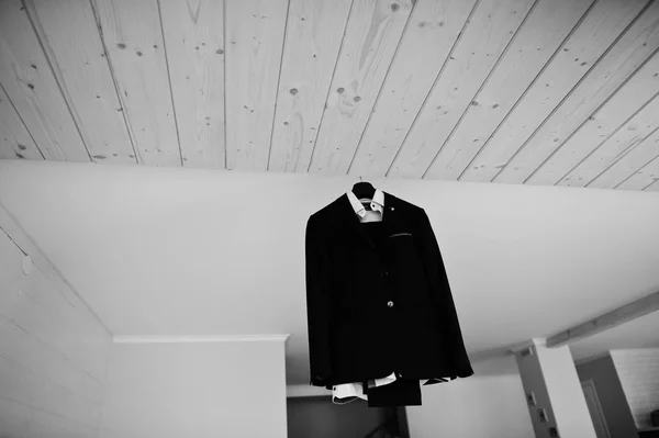 Groom\'s wedding suit hanging on the rack in big light room. Blac