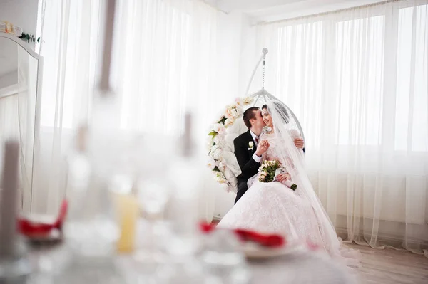 Wedding couple sitting on the floral swing in the studio. — Stock Photo, Image