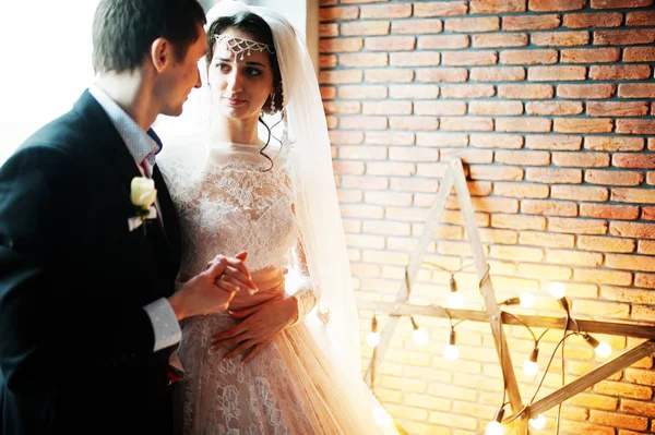 Свадебная пара позирует против кирпичной стены со звездообразным светом . — стоковое фото