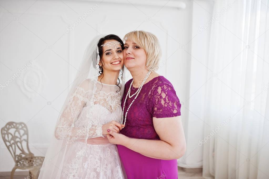 Lovely bride in wedding gown posing with her mother in purple lo