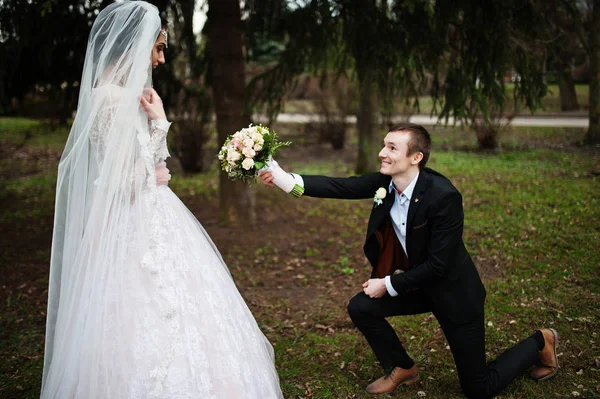 Beau marié agenouillé avec un bouquet dans le parc devant un — Photo