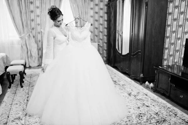 Портрет красивой невесты, позирующей с платьем на вешалке — стоковое фото