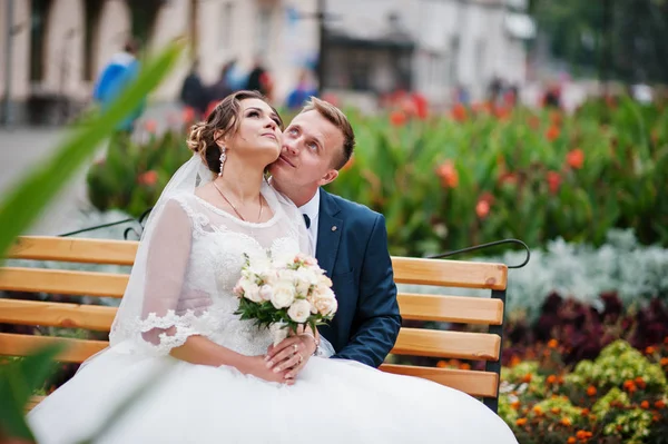 Elegant wedding couple sitting on a bench in the park and lookin — Stock Photo, Image