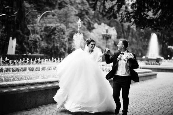 Couple de mariage marche et sourire sur le trottoir avec une fontaine i — Photo