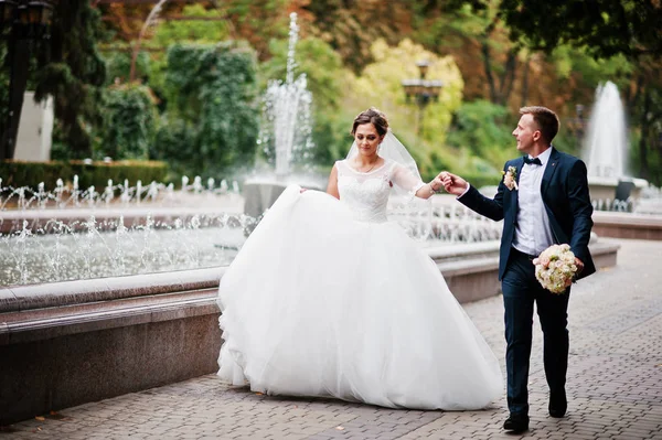 Wedding couple walking and smiling on pavement with a fountain i — Stock Photo, Image