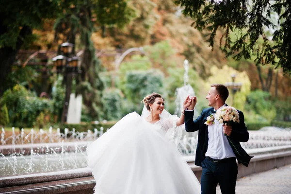 Bröllop par promenader och leende på trottoaren med en fontän i — Stockfoto