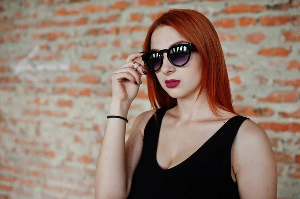 Menina de cabelo vermelho elegante em óculos de sol desgaste em preto, contra aba — Fotografia de Stock