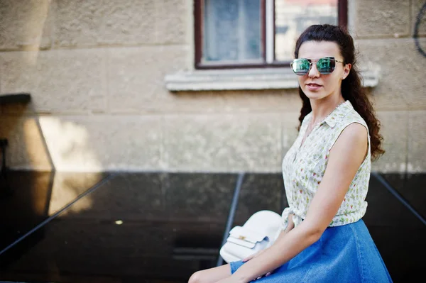 Lockiges stylisches Mädchen trägt blauen Jeansrock, Bluse und Sonnenbrille — Stockfoto