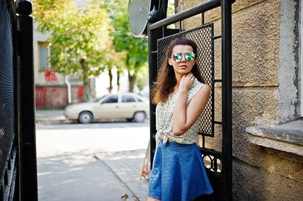 Кудрявая стильная девушка одевается в джинсовые юбки, блузку и солнцезащитные очки — стоковое фото