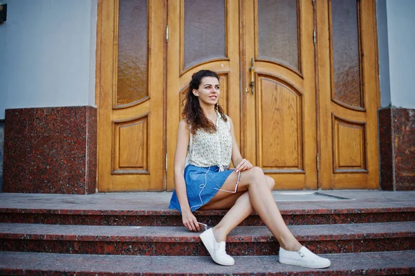 Krullend stijlvolle meisje slijtage van blue jeans rok, blouse en listenin — Stockfoto