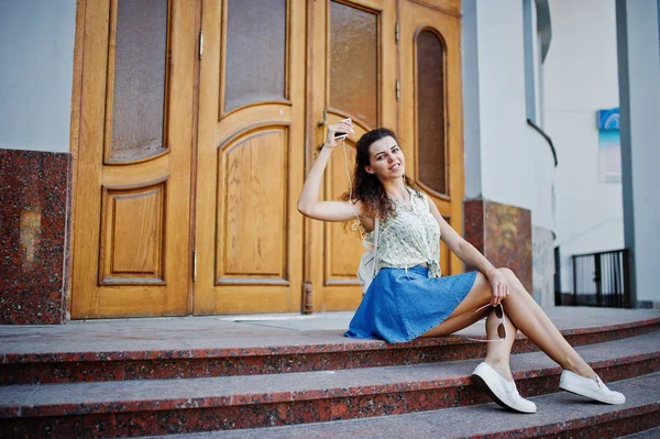Lockiges stylisches Mädchen trägt blauen Jeansrock, Bluse und Hörerin — Stockfoto
