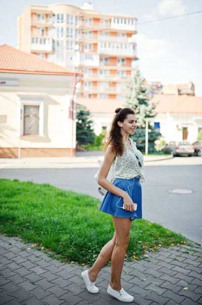 Lockiges stylisches Mädchen trägt blauen Jeansrock, Bluse und Hörerin — Stockfoto