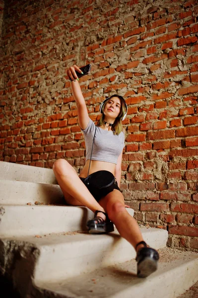 Menina desgaste em shorts com fones de ouvido grandes fazer selfie em abadoned — Fotografia de Stock