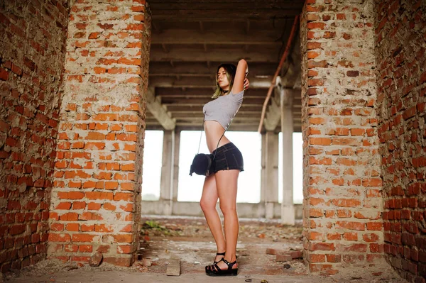 Flicka bära på shorts på abadoned fabrikens med tegelväggar. — Stockfoto