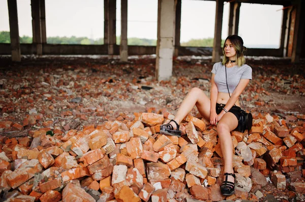 Flicka bära på shorts på abadoned fabrikens sitter på tegel. — Stockfoto