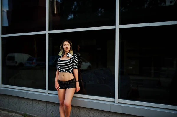 Girl wear on shorts with big headphones against large windows bu — Stock Photo, Image