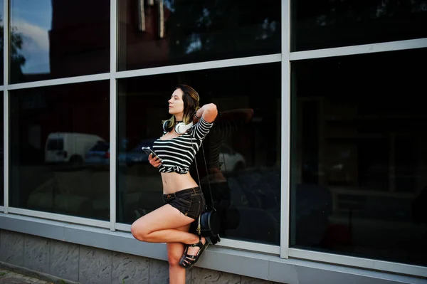 Menina desgaste em shorts com fones de ouvido grandes contra grandes janelas bu — Fotografia de Stock