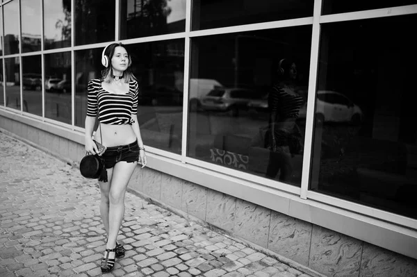 Chica llevar en pantalones cortos con auriculares grandes contra grandes ventanas bu —  Fotos de Stock